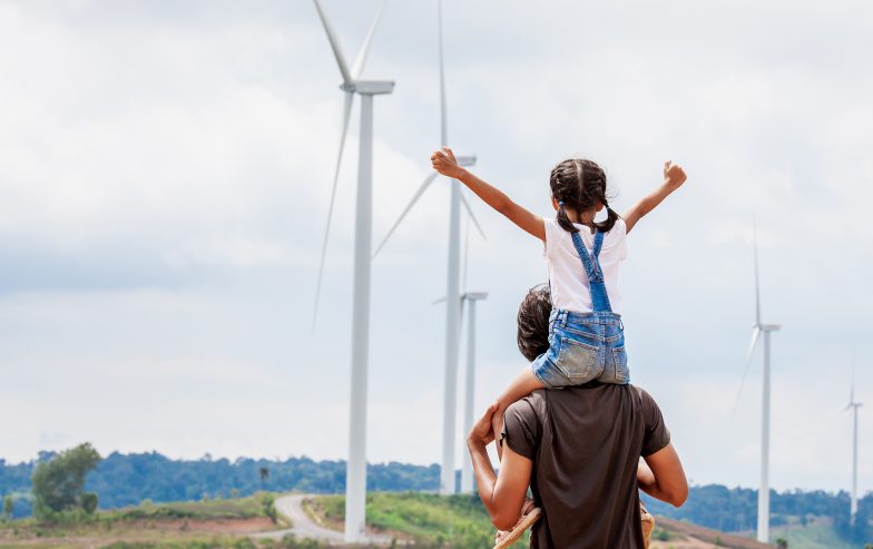 A man with a child on his shoulders, looking at wind tourbines