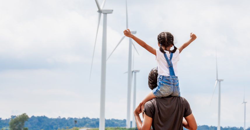 A man with a child on his shoulders, looking at wind tourbines