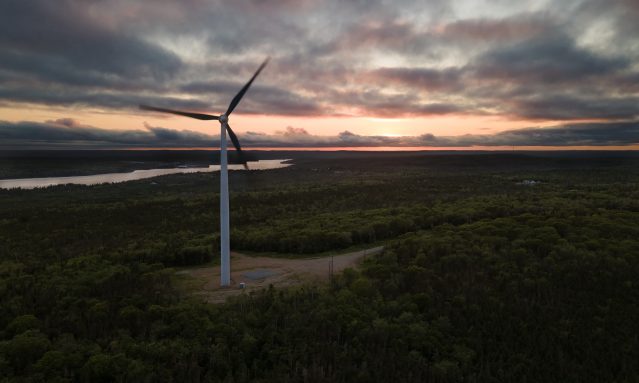 a wind turbine standing in a field with a sunrise