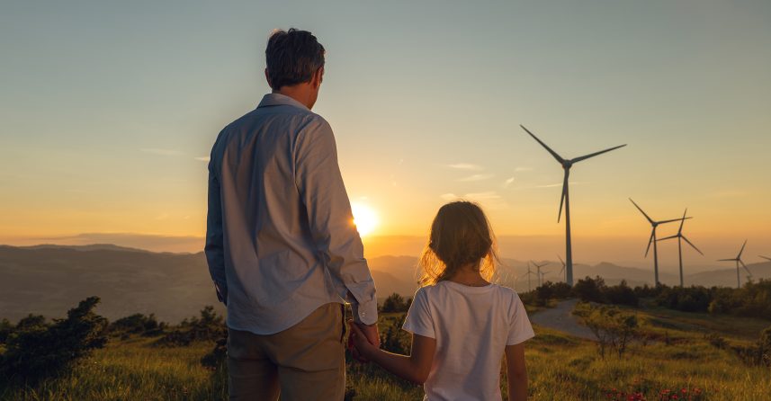 man and young child holding hands look at wind turbines