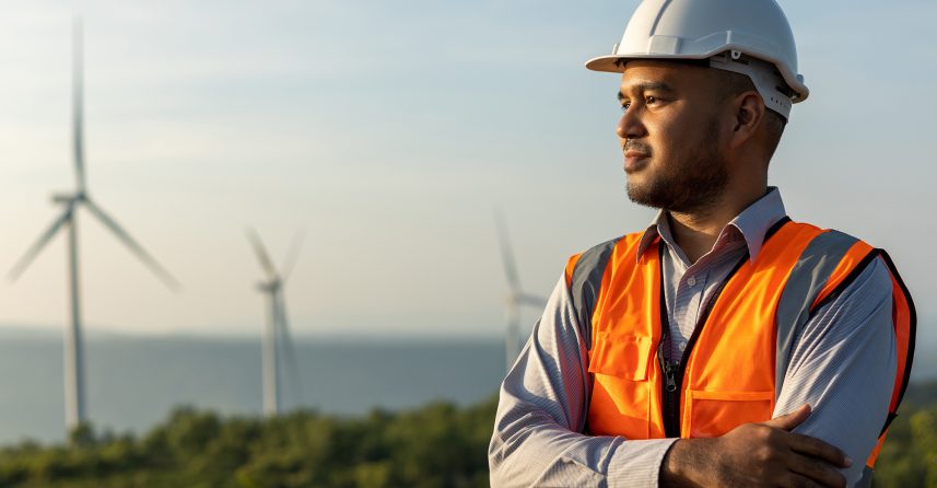 Man in a hard hard hat and safety vest standing in front of wind turbines